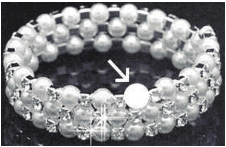 Fotografia original da pulseira de pérolas, com seta branca indicando a posição da pérola faltante.