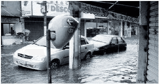 Fotografia de inundação urbana, automóveis e telefone público; não contém manchete independente.
