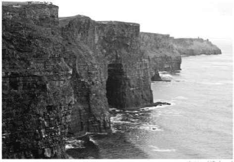 Fotografia de uma costa com paredes rochosas altas e íngremes e mar junto à sua base.
