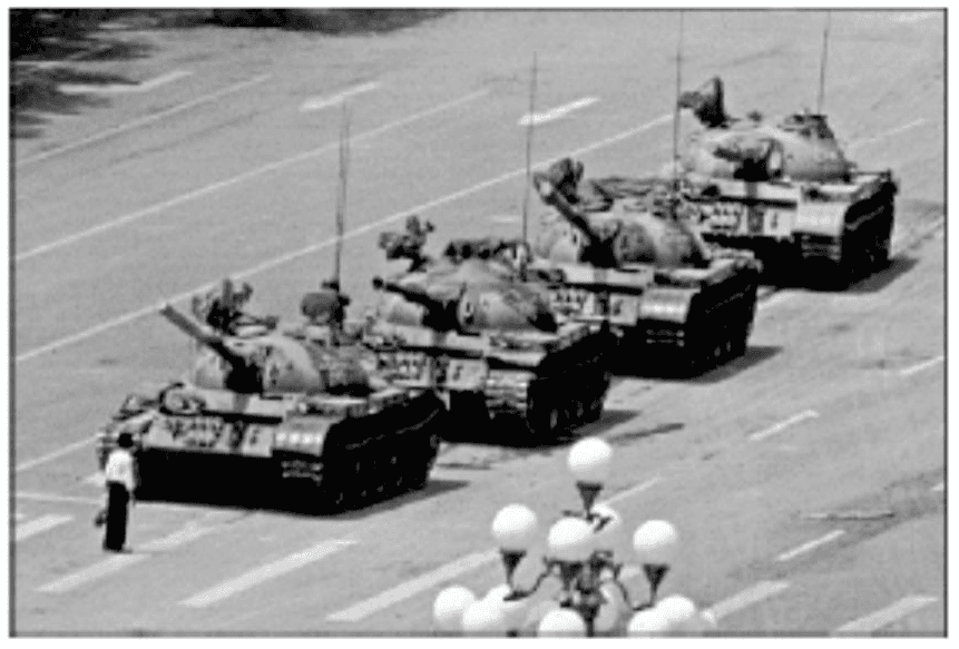 Fotografia de um homem diante de uma coluna de quatro tanques em Beijing, China, em 1989. Preservados limites da fotografia, pista, veículos e luminárias; sem crédito impresso na fonte.