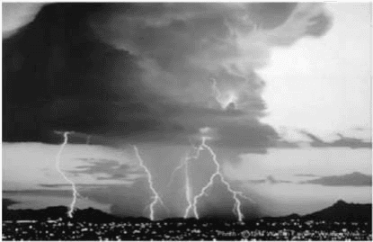 Fotografia de tempestade com nuvens e relâmpagos sobre área urbanizada.