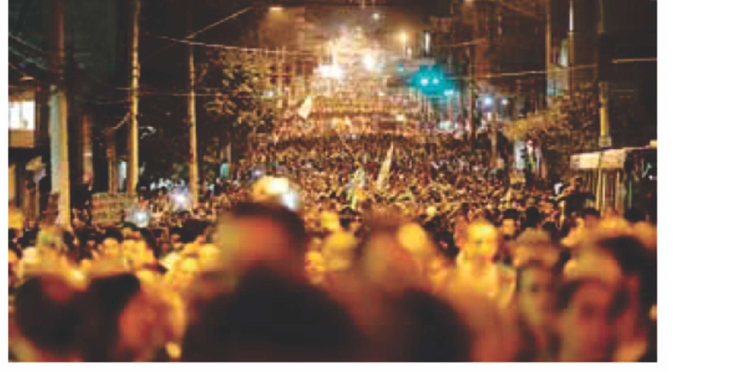 Fotografia noturna de uma manifestação que ocupa uma rua.